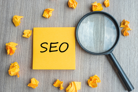 SEO (Search Engine Optimization) words on yellow note with crumbled paper and magnifying glass on wooden table background. Idea, Vision, Strategy, Analysis, Keyword and Content conceptの写真素材