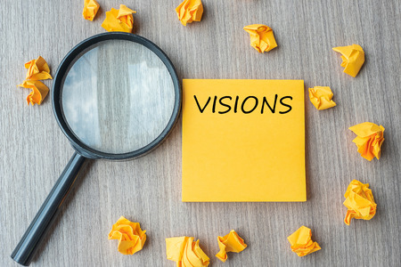 vision words on yellow note with crumbled paper and magnifying glass on wooden table background. SEO, Idea, goal, Strategy, Analysis, Keyword and Content conceptの写真素材