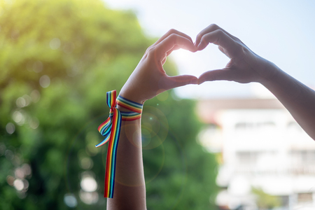 woman hands showing heart shape sign with LGBTQ Rainbow ribbon in the morning for Lesbian, Gay, Bisexual, Transgender and Queer communityの写真素材