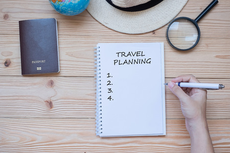 hand traveler writing Travel planning word on notebook with accessories, Camera, Passport, Magnifying, smart Phone and hat on wooden table, Top view and copy space.の写真素材