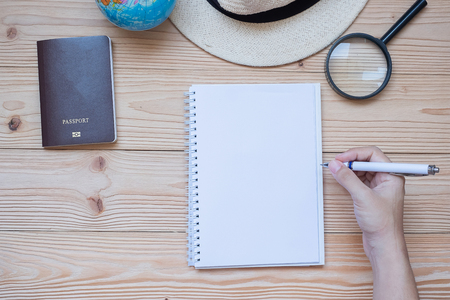 hand traveler writing  on notebook with accessories, Camera, Passport, Magnifying, smart Phone and hat on wooden table, Top view and copy space. Travel planning conceptの写真素材