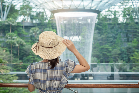 young woman wear blue dress and hat, Asian traveler standing and looking to beautiful rain vortex at Jewel Changi Airport, landmark and popular for tourist attractions in Singapore. Travel conceptのeditorial素材