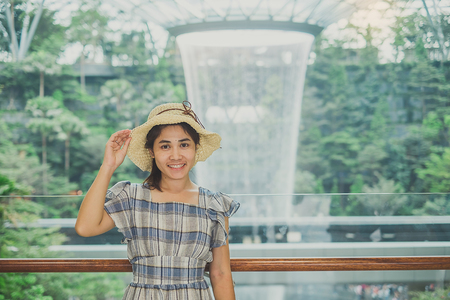 young woman wear blue dress and hat, Asian traveler standing and looking to beautiful rain vortex at Jewel Changi Airport, landmark and popular for tourist attractions in Singapore. Travel conceptのeditorial素材
