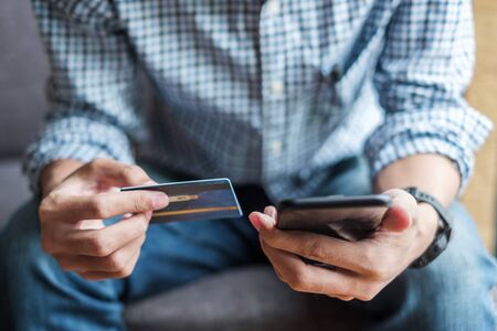 Young casual Business man holding credit card and using touchscreen smartphone for online shopping while making orders in the cafe.business, lifestyle, technology, ecommerce and online payment conceptの写真素材