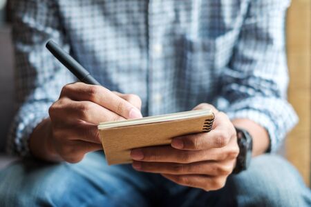 Businessman writing something on notebook in office, hand of man holding pen with signature on paper report. business conceptsの写真素材