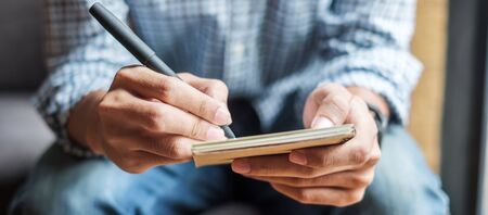 Businessman writing something on notebook in office, hand of man holding pen with signature on paper report. business conceptsの写真素材