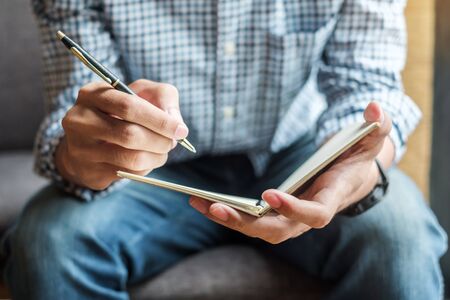 Businessman writing something on notebook in office, hand of man holding pen with signature on paper report. business conceptsの写真素材