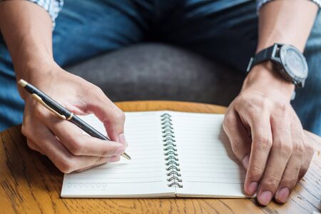 Businessman writing something on notebook in office, hand of man holding pen with signature on paper report. business conceptsの写真素材