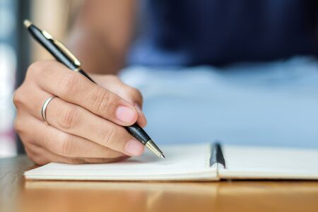 Businesswoman writing something on notebook in office, hand of woman holding pen with signature on paper report. business conceptsの写真素材