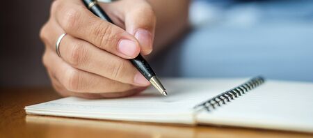 Businesswoman writing something on notebook in office, hand of woman holding pen with signature on paper report. business conceptsの写真素材
