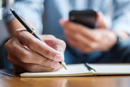 Young casual Business man writing something on notebook and using touchscreen smartphone in the cafe. business, lifestyle, technology conceptの写真素材