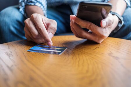 Young casual Business man holding credit card and using touchscreen smartphone for online shopping while making orders in the cafe.business, lifestyle, technology, ecommerce and online payment conceptの写真素材