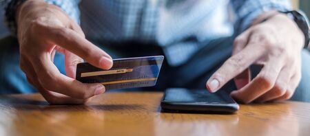 Young casual Business man holding credit card and using touchscreen smartphone for online shopping while making orders in the cafe.business, lifestyle, technology, ecommerce and online payment conceptの写真素材