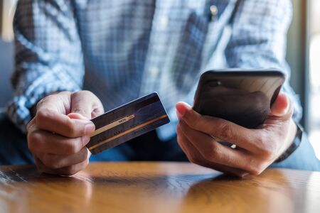 Young casual Business man holding credit card and using touchscreen smartphone for online shopping while making orders in the cafe.business, lifestyle, technology, ecommerce and online payment conceptの写真素材