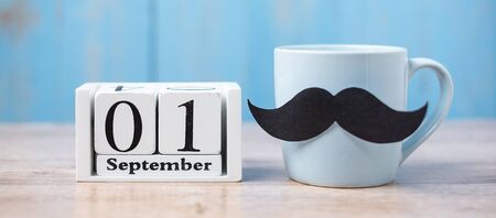Blue coffee cup with Black moustache and 1 September Calendar on wood table background in the morning. Father, International men day, Prostate Cancer Awareness and World cancer day conceptの写真素材