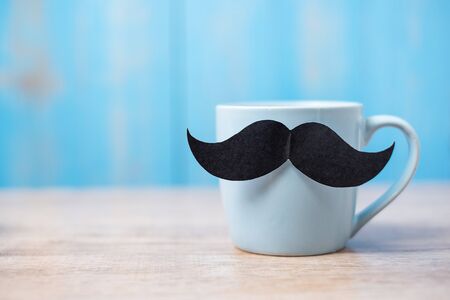Blue coffee cup with Black moustache on wood table background in the morning. Father, International men day, Prostate Cancer Awareness and World cancer day conceptの写真素材
