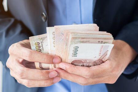 Businessman hand holding Thai Baht banknote stack. business, money, investment, finance and payment conceptsの写真素材