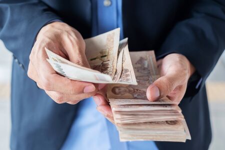 Businessman hand holding Thai Baht banknote stack. business, money, investment , finance and payment conceptsの写真素材