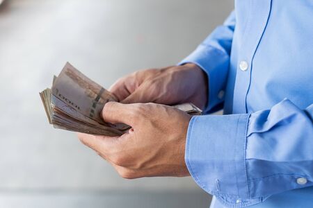 Businessman hand holding Thai Baht banknote stack. business, money, investment, finance and payment conceptsの写真素材