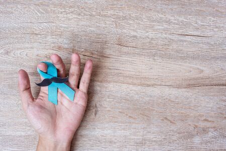 Prostate Cancer Awareness, Man holding light Blue Ribbon with moustache on wooden background for supporting people living and illness. Men Healthcare and World cancer day conceptの写真素材