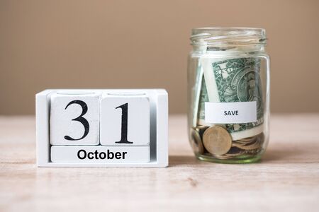 31 October of calendar wooden and money in glass jar on table, world saving day, business,...