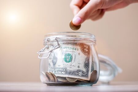 Woman hand putting coin money in glass jar. world saving day, business, investment, retirement planning, finance conceptの写真素材