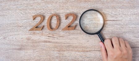 2020 Happy New year with Businessman holding glass magnifying and wooden number on table. New Start,...