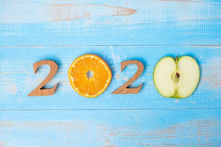 2020 Happy New Year and New You with green apple and Orange fruits on blue wood background. Goals,...