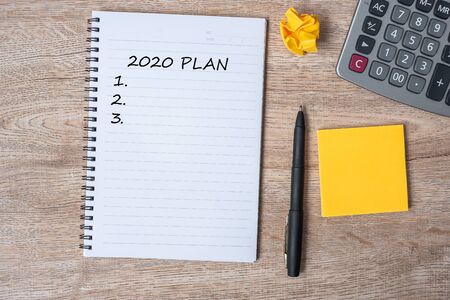2020 NEW YEAR PLAN word on note with pen and crumbled paper on wooden table background. NEW START,...