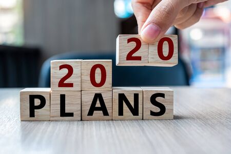 Business man hand holding wooden cube with 2020 Plans word on table background. Resolution, strategy, solution, goal, business and New Year holiday conceptsの写真素材