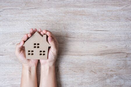 Hands holding house model on wood table background with copy space. Financial, money, refinance, Real estate and new home conceptの写真素材