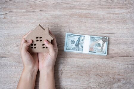 Man hands holding Wood house model beside money of American dollar banknote. real estate, Property investment, home mortgage financial and savings conceptsの写真素材