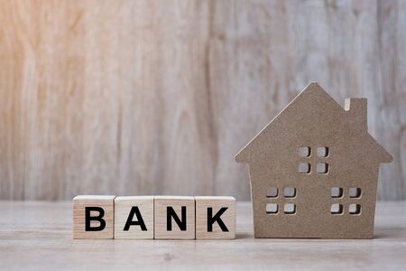 Wood block with BANK text and house model on wooden background. Banking, real estate, Property investment, home mortgage, financial and savings conceptsの写真素材