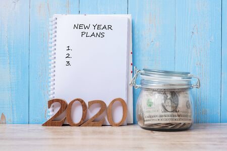 2020 New Year Plans word on notebook, money glass jar and wooden number. financial, Resolution, Goals, Action and saving Conceptの写真素材