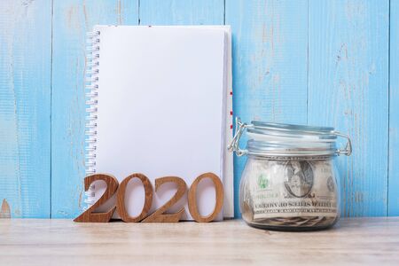 2020 New Year with blank notebook, money glass jar and wooden number. financial, Resolution, Goals, Plan, Action and saving Conceptの写真素材