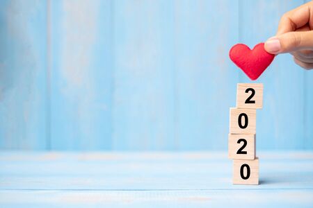 Business man hand holding red heart shape over 2020 wooden cubes on blue table background with copy space for text. Business, Resolution, New Year New You and Happy Valentineâs day holiday conceptの写真素材