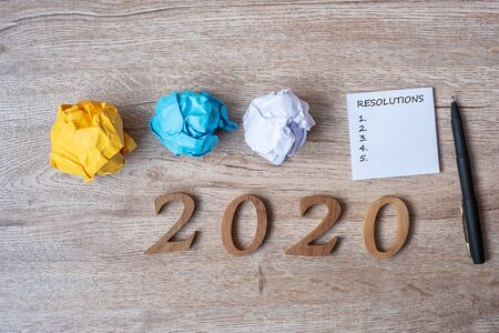 2020 NEW YEAR RESOLUTION word on yellow note with pen and crumbled paper on wooden table background. NEW START, Strategy and Goal conceptの写真素材