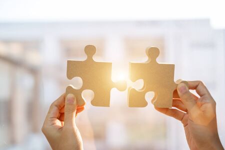 Woman hands connecting couple puzzle piece against sunrise effect, businesswoman holding wood jigsaw...