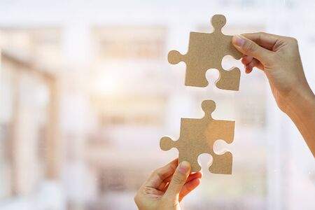Woman hands connecting couple puzzle piece against sunrise effect, businesswoman holding wood jigsaw with sunset background. Business solutions, target, success, goals and strategy conceptsの写真素材