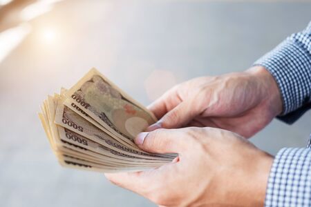 Businessman hand holding Japanese Yen banknote stack. business, money, investment , finance and payment conceptsの写真素材