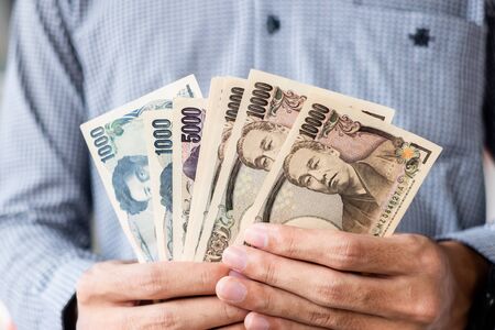 Businessman hand holding Japanese Yen banknote stack. business, money, investment , finance and payment conceptsの写真素材