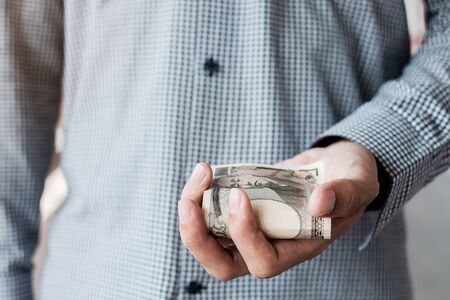 Businessman hand holding Japanese Yen banknote stack. business, money, investment, finance and payment conceptsの写真素材