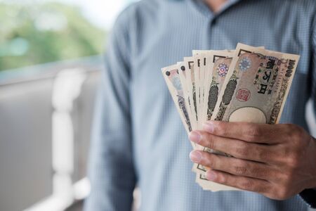 Businessman hand holding Japanese Yen banknote stack. business, money, investment, finance and payment conceptsの写真素材