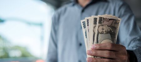 Businessman hand holding Japanese Yen banknote stack. business, money, investment, finance and payment conceptsの写真素材