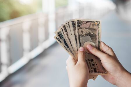 Businessman hand holding Japanese Yen banknote stack. business, money, investment, finance and payment conceptsの写真素材