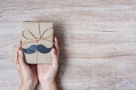 holding gift box with mustache on wooden background, preparation for fathers. World International men day and Fatherâs day conceptの写真素材