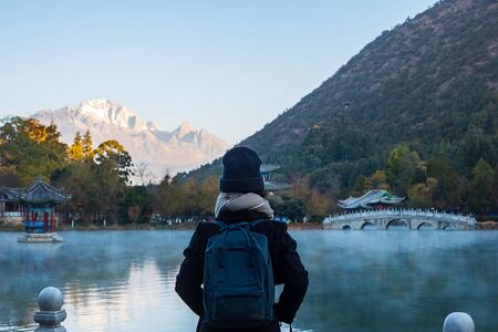 Young woman traveler traveling at Black Dragon Pool with Jade Dragon Snow Mountain background, landmark and popular spot for tourists attractions near Lijiang Old Town. Lijiang, Yunnan, Chinaの写真素材
