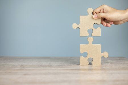 Man connecting couple puzzle piece, wood jigsaw on table  background. Business solutions, mission, success, goals and strategy conceptsの写真素材