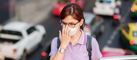 young Asian woman wearing N95 respiratory mask protect and filter pm2.5 (particulate matter) against traffic and dust city. healthcare and air pollution conceptの写真素材