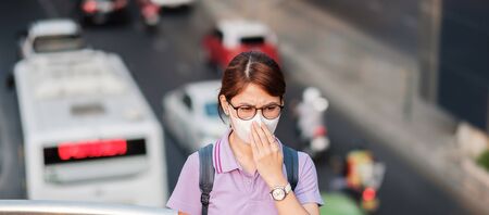 young Asian woman wearing N95 respiratory mask protect and filter pm2.5 (particulate matter) against traffic and dust city. healthcare and air pollution conceptの写真素材